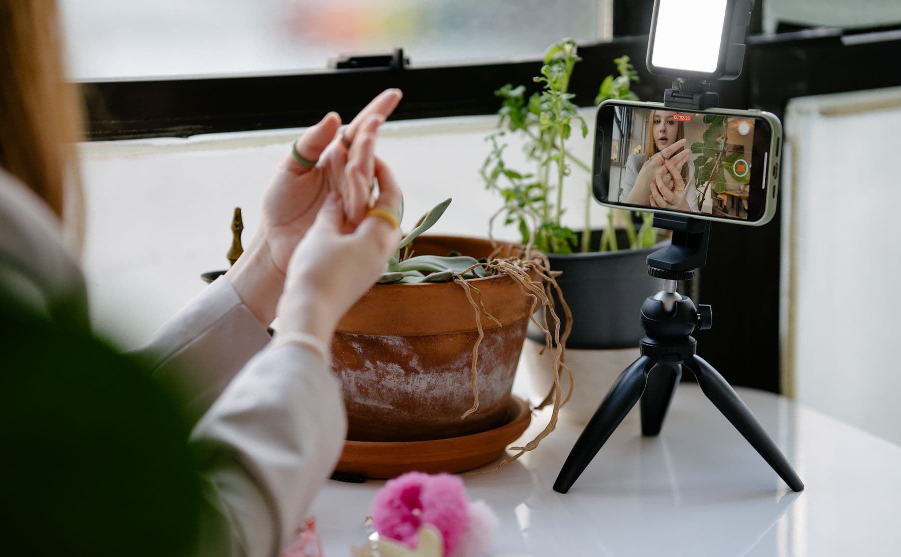 A creator filming herself at home with her phone on a tripod, seen from behind